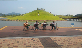4명의 남성이 봉화언덕을 배경으로 기타를 치며 노래하고 있다.